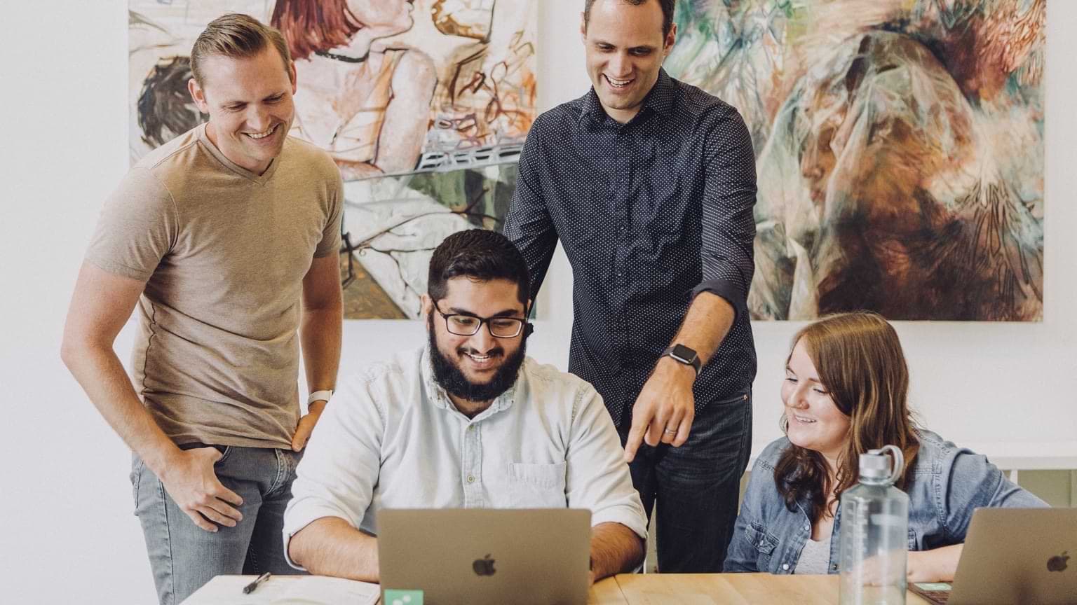Four colleagues around one laptop, laughing